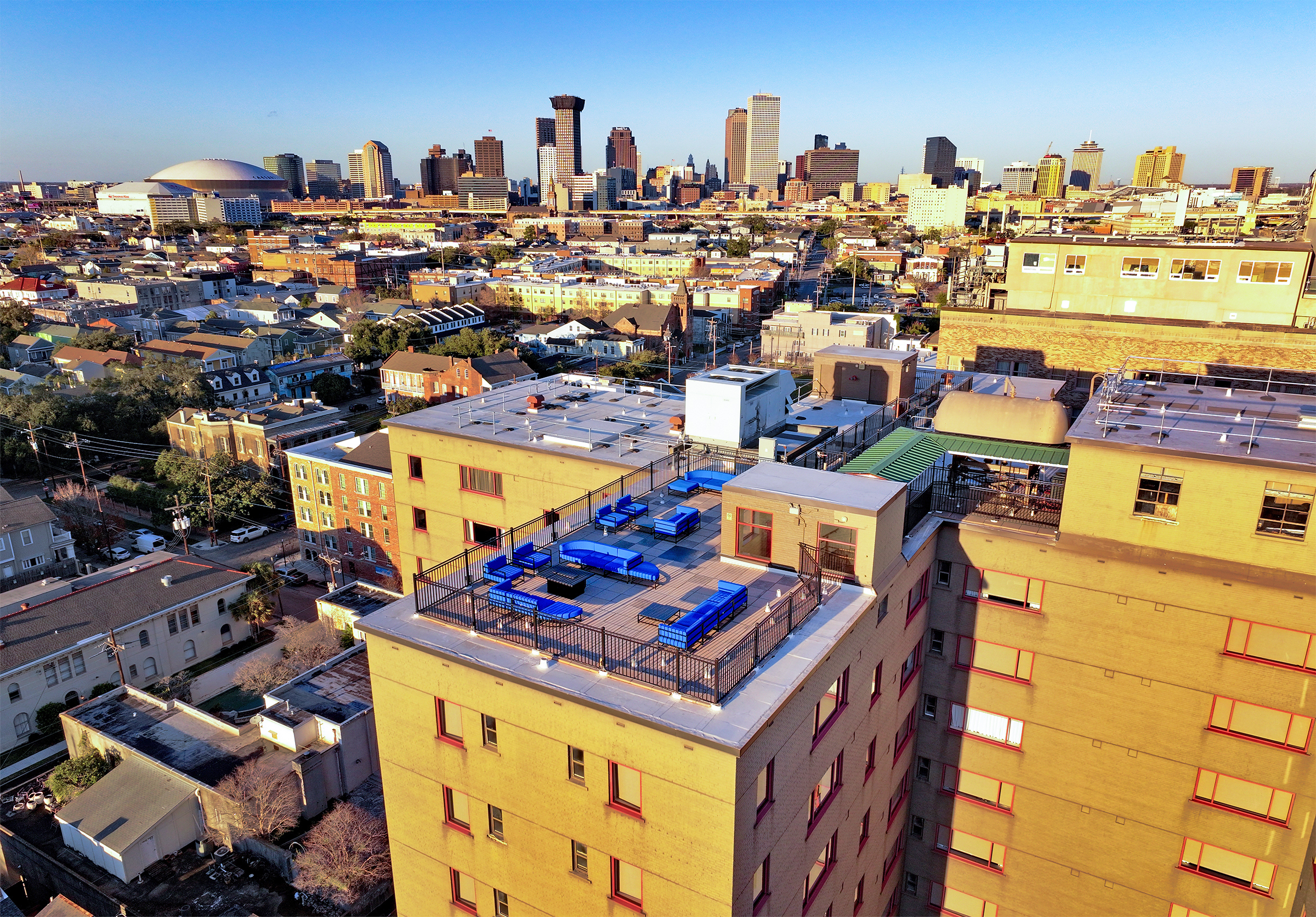 Aerial view of a yellow building with a rooftop patio featuring blue lounge chairs and a city skyline in the background.